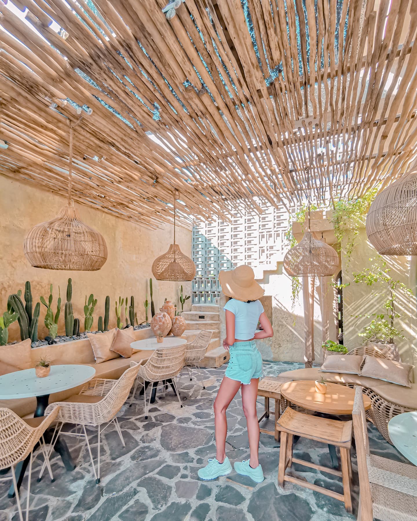 Stylish cafe patio with bamboo ceiling, hanging lamps, and cacti decor.