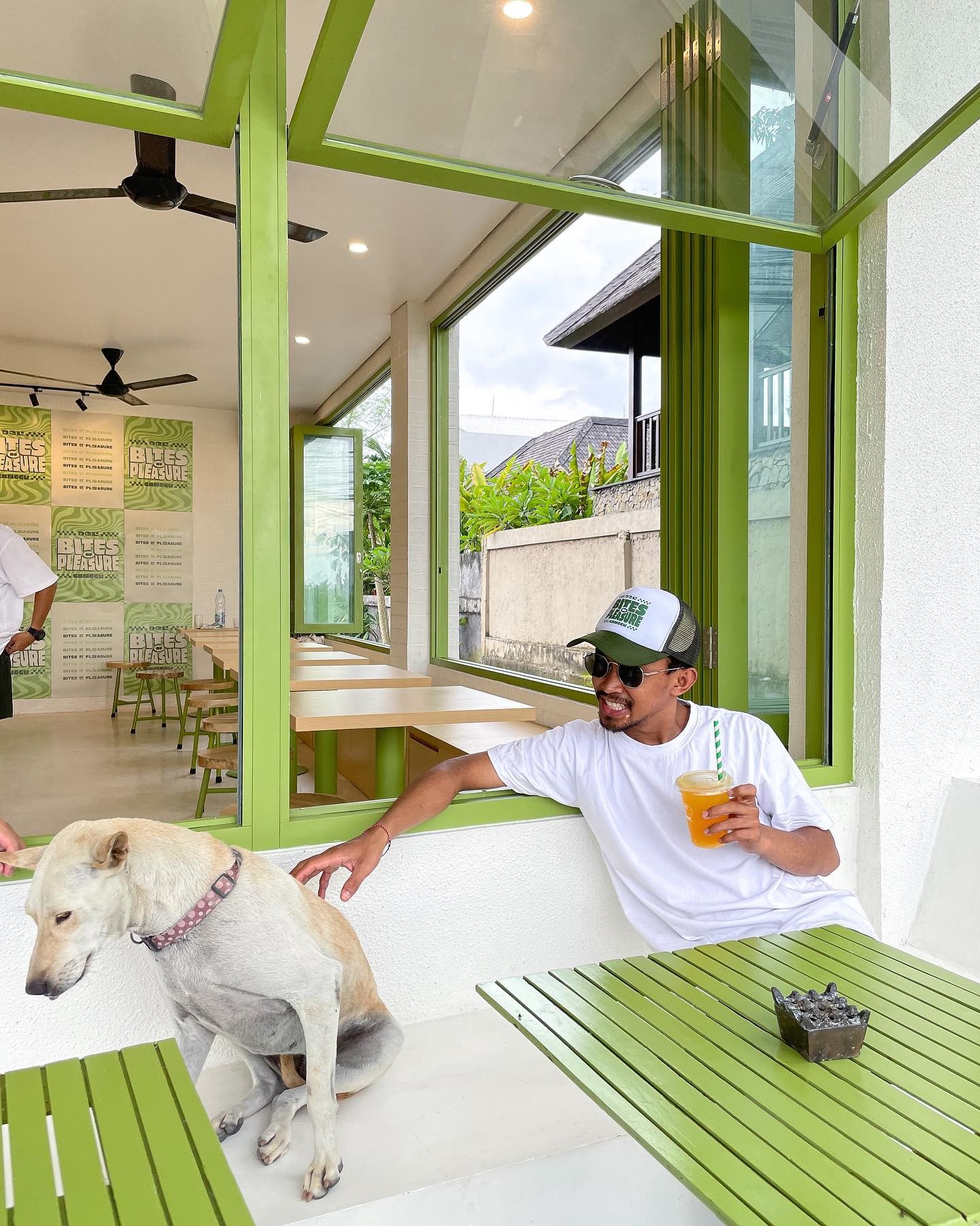 Bright cafe interior with green frames, white walls decorated with neon prints, and outdoor seating area with green tables.